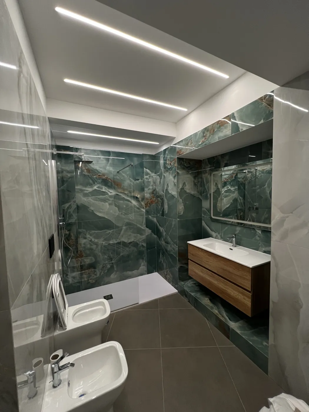 Bagno in gres effetto onice verde con tagli di luce LED a soffitto, Roma Piazza Fiume